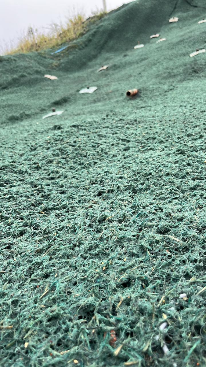 Detalhe da biomanta verde de fibra aplicada sobre talude após hidrossemeadura
